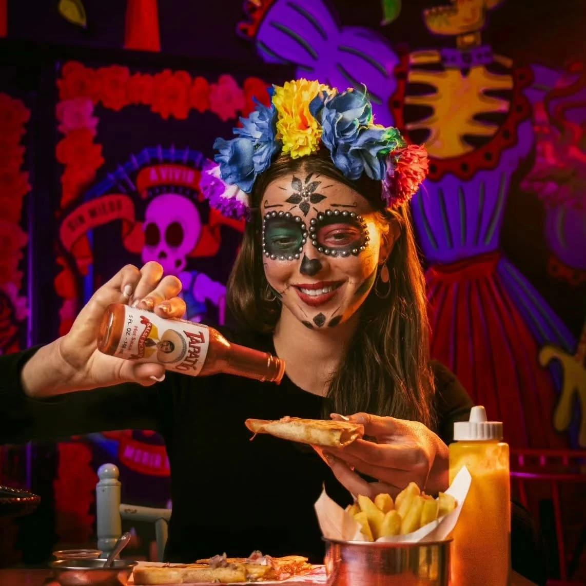 Chica maquillada de catrina poniendo salsa picante a su quesadilla