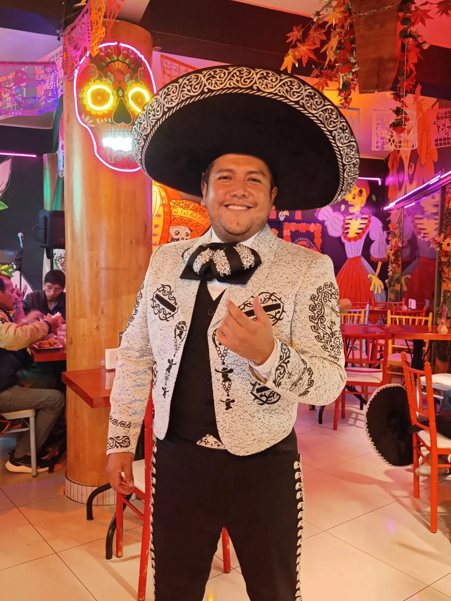 Mariachi sonriente en el salón, con la calavera de neón detrás